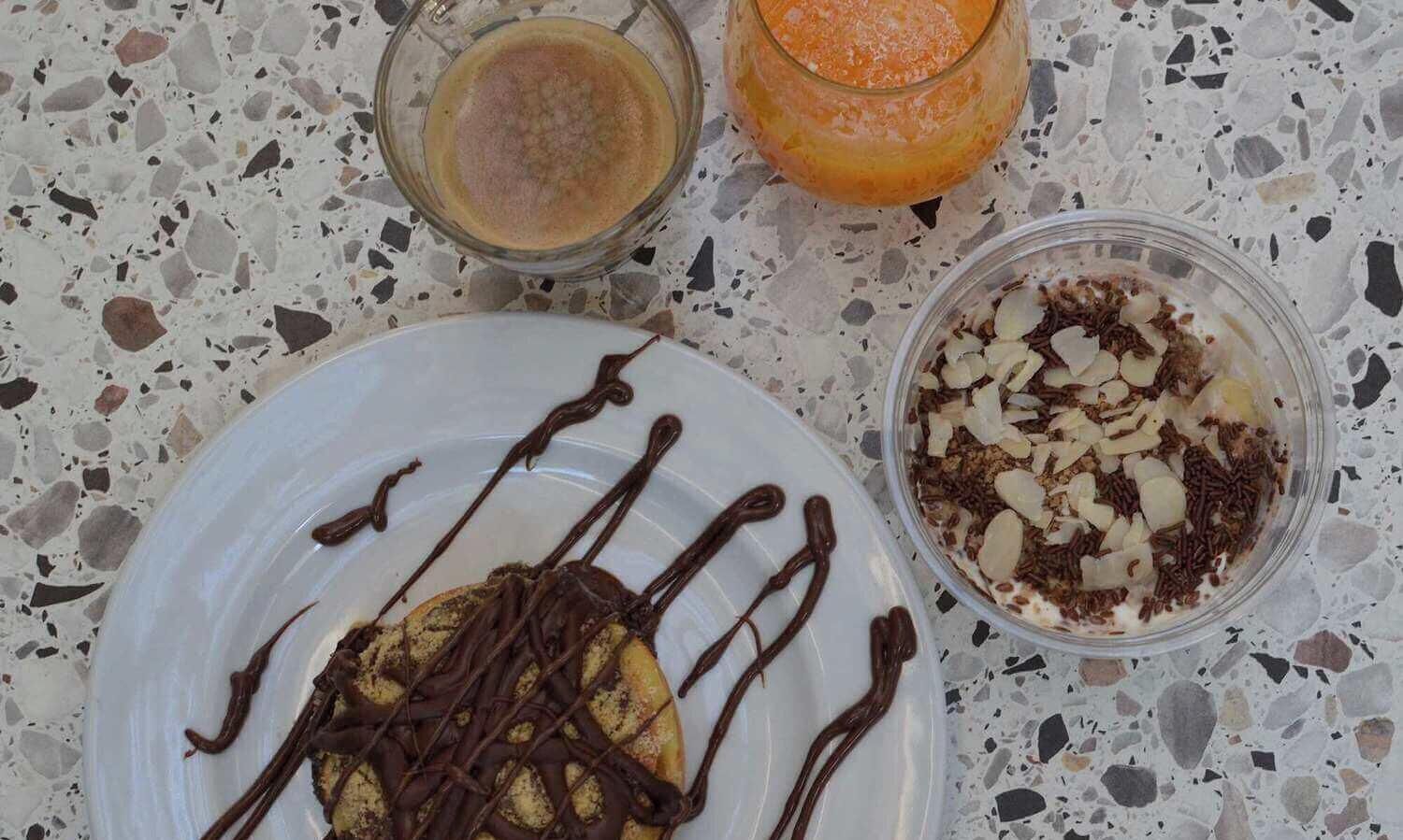 Ein Teller mit Dessert, ein Glas Orangensaft und eine Schüssel Müsli mit Mandeln.