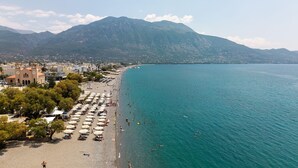 Une plage avec des parasols et des gens, une montagne en arrière-plan et des bâtiments le long de la côte.