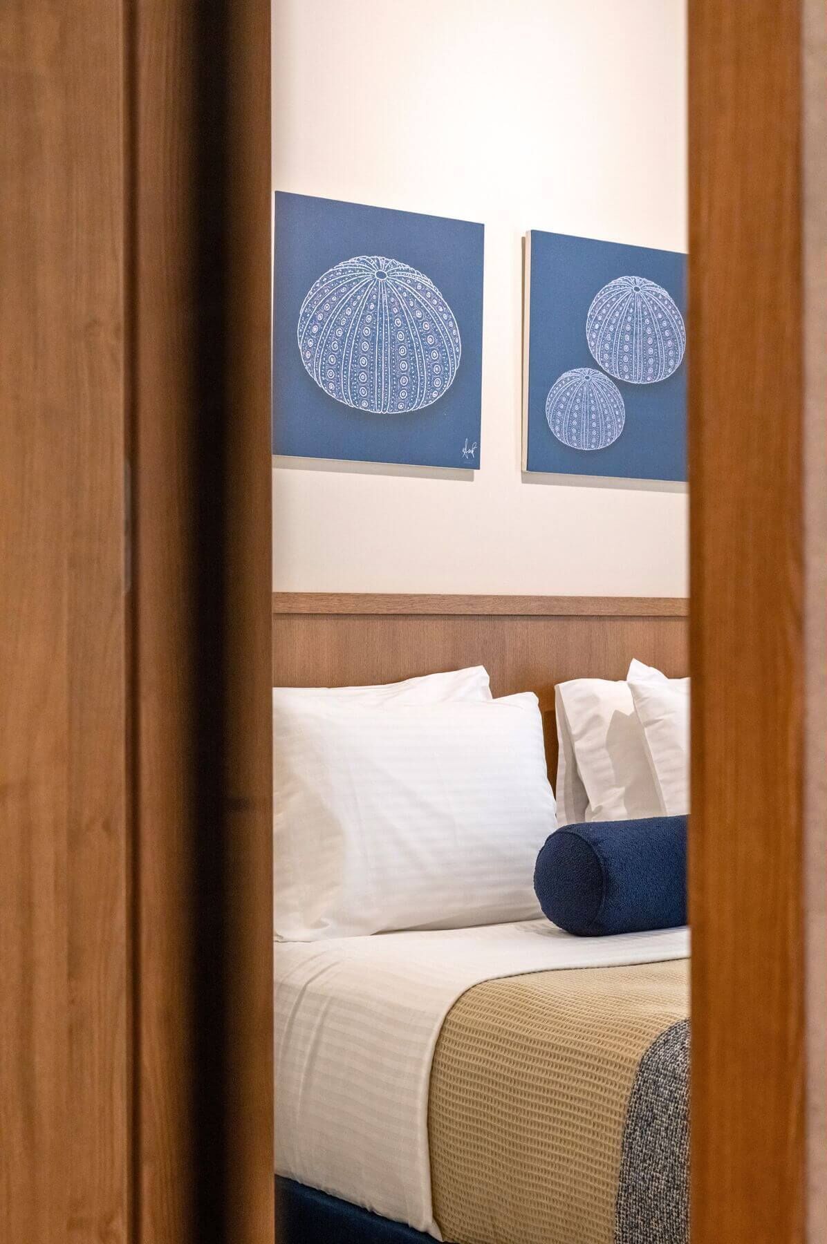 Habitación de hotel con una cama, almohadas blancas y azules, una colcha azul y dos cuadros en la pared.