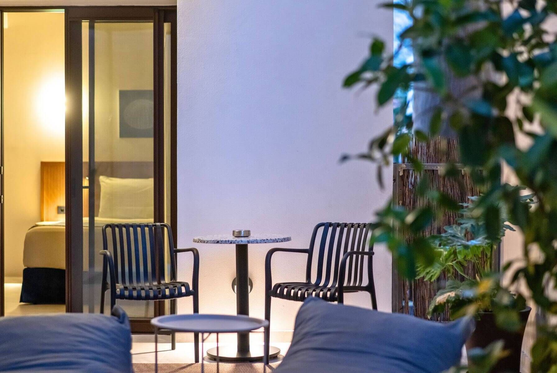 A hotel room with a bed, a small table, two chairs, and a view of the outside.