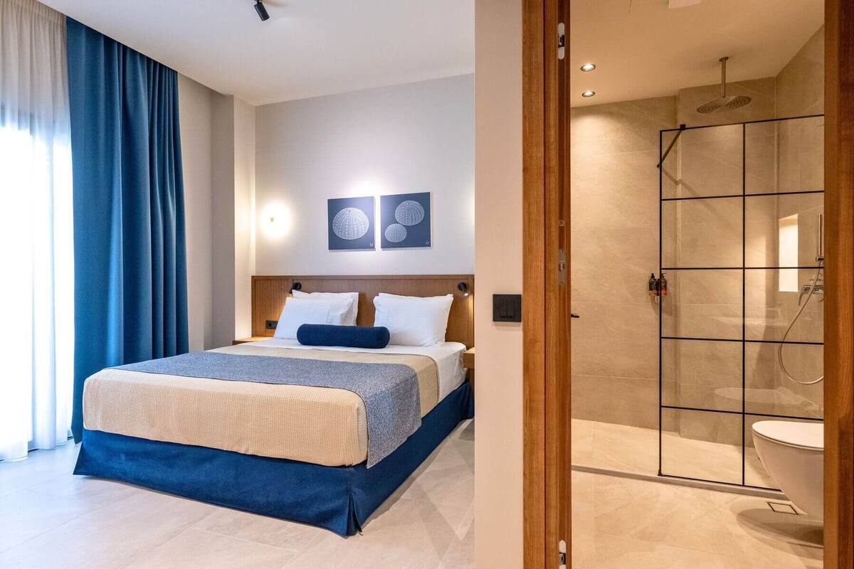 Habitación de hotel con una cama grande, ducha con puerta de vidrio y vistas al mar.