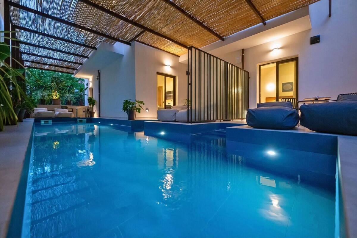 Una piscina interior con techo de paja, zonas de estar y plantas en macetas.