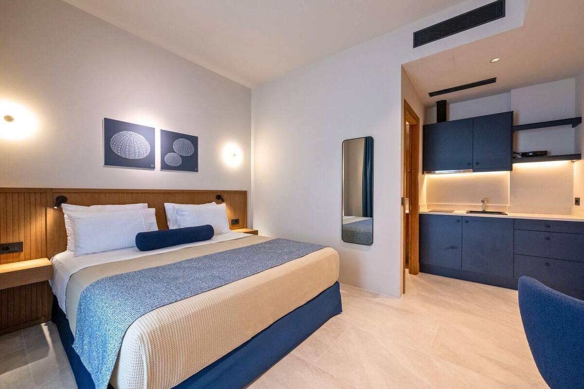 Una habitación de hotel moderna con cama, mesitas de noche, un espejo y una kitchenette.