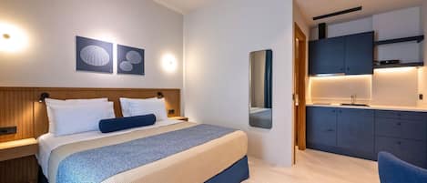 A modern hotel room with a bed, bedside tables, a mirror, and a kitchenette.