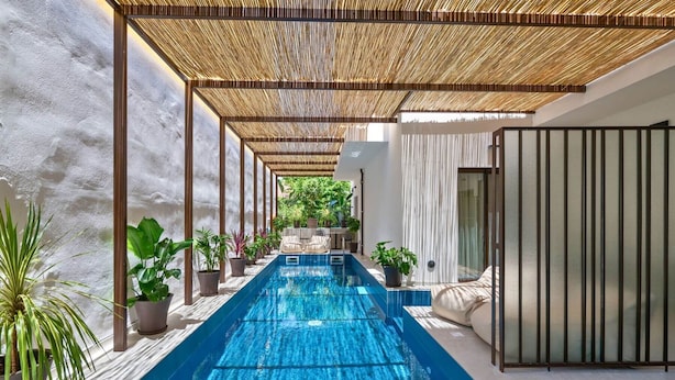 Un espace piscine intérieur moderne, doté d’un long bassin rectangulaire, entouré de plantes en pot et agrémenté d’un espace détente abrité.