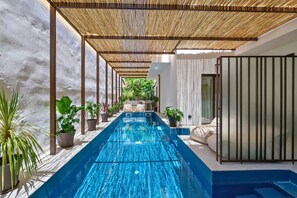 A modern indoor pool area with a long, narrow pool, surrounded by potted plants and a covered seating area. - Achinos - Kalamata Mediterranean Suites (Kalamata)