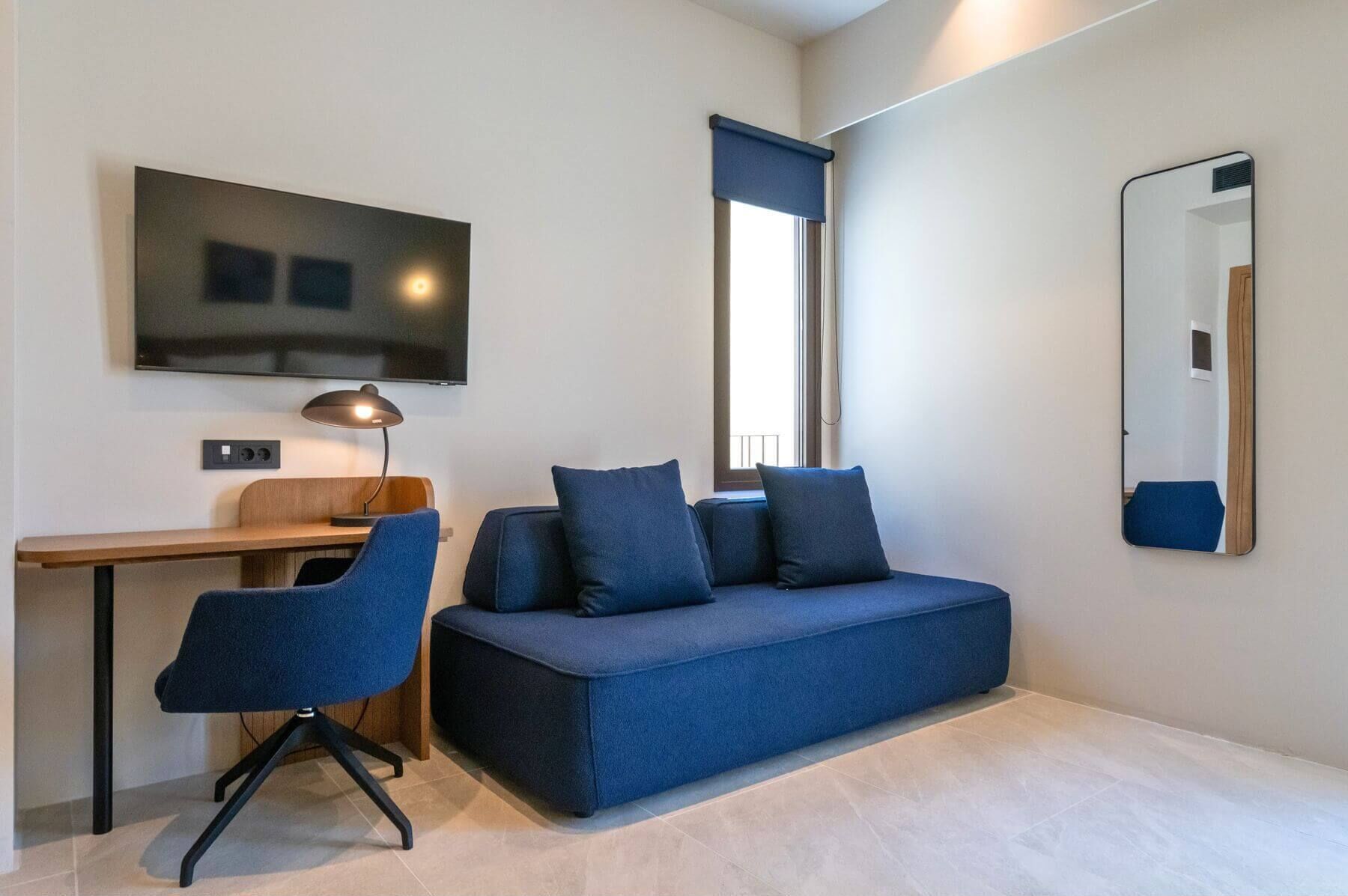 Habitació moderna amb un sofà, una taula de treball, una cadira, un televisor i un mirall.