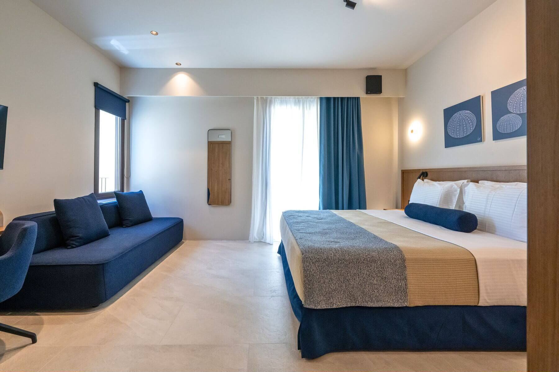 Una habitación de hotel moderna con cama, sofá, espejo y televisor de pared.