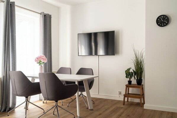 A modern living room with a flat-screen TV mounted on the wall, a wooden floor, and a small wooden stool with potted plants.