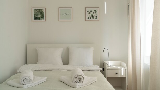 A neatly made bed with two pillows, a bedside table with a lamp, and three framed pictures on the wall. - RentPlanet - Apartament Stawowa (Wroclaw)