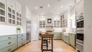 Une cuisine avec des meubles blancs, une table en bois et une horloge au mur.