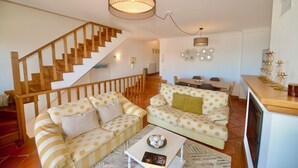 A living room with two sofas, a coffee table, a staircase, and a dining area. - Collasão - Stunning Duplex with Pool & Sea Views (São Martinho do Porto)