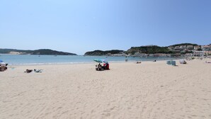 A beach with umbrellas, a few people, and buildings in the background. - Collasão - Stunning Duplex with Pool & Sea Views (São Martinho do Porto)