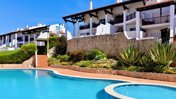A swimming pool with a stone wall and a building with balconies in the background. - Collasão - Stunning Duplex with Pool & Sea Views (São Martinho do Porto)