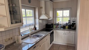 A kitchen with white cabinets, a granite countertop, a built-in oven, a sink, and a window with a view of greenery.