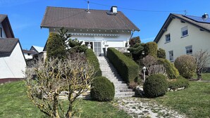 A two-story house with a front yard, a stone staircase, and a statue.