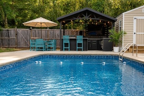 Une piscine avec un patio couvert, un espace salon extérieur et un barbecue.