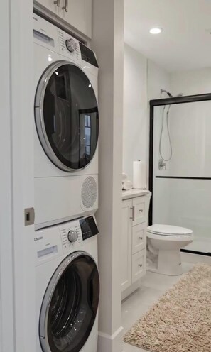 Une buanderie moderne équipée de machines à laver et de sèche-linge superposés, de toilettes et d’une douche.