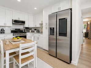 Une cuisine moderne avec des meubles blancs, des appareils en acier inoxydable et une table à manger en bois.