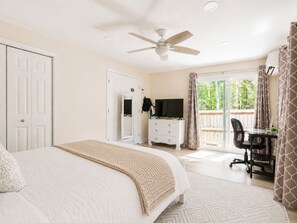 Un dormitorio con cama, escritorio, silla, ventilador de techo y vistas al exterior.