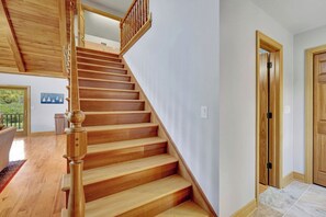 A wooden staircase leading to an upper floor, a door with a wooden frame, and a view of a room with a window and a door.