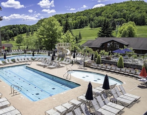 A pool area with lounge chairs, a water slide, and a view of a green landscape.