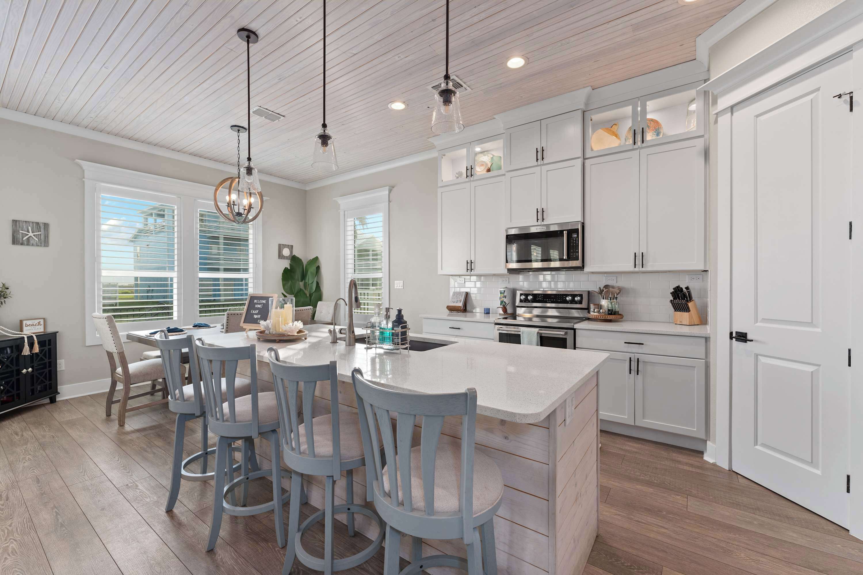 Une cuisine moderne avec des meubles blancs, un grand îlot central et des luminaires suspendus.