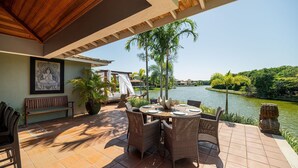 An outdoor patio with a round table and chairs, a bench, and a view of a lake. - Bz58 Casa Piscina privativa e vista lago (Buzios)