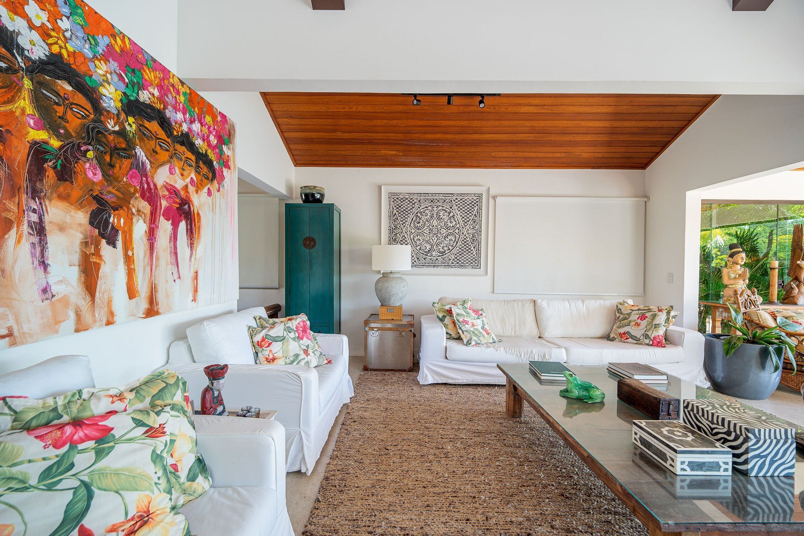 Un moderno salón con sofás blancos, un cuadro floral grande, techo de madera y vistas a zonas verdes.