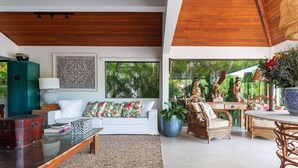 A spacious living area with a white sofa, a wooden coffee table, wicker furniture, and a large window offering a view of tropical greenery. - Bz58 Casa Piscina privativa e vista lago (Buzios)