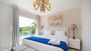 A modern bedroom with a large bed, a chandelier, and a view of greenery outside. - Bz58 Casa Piscina privativa e vista lago (Buzios)