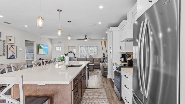 A modern kitchen with a large stainless steel refrigerator, white cabinetry, and pendant lighting. - 218 Oasis On Ohio: Stunning Pool Home W/ Dock Access! 3 Bedroom Home (Fort Myers Beach)