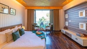 Habitación de hotel con una cama grande, techo de madera, un balcón con sillas y un televisor montado en la pared.