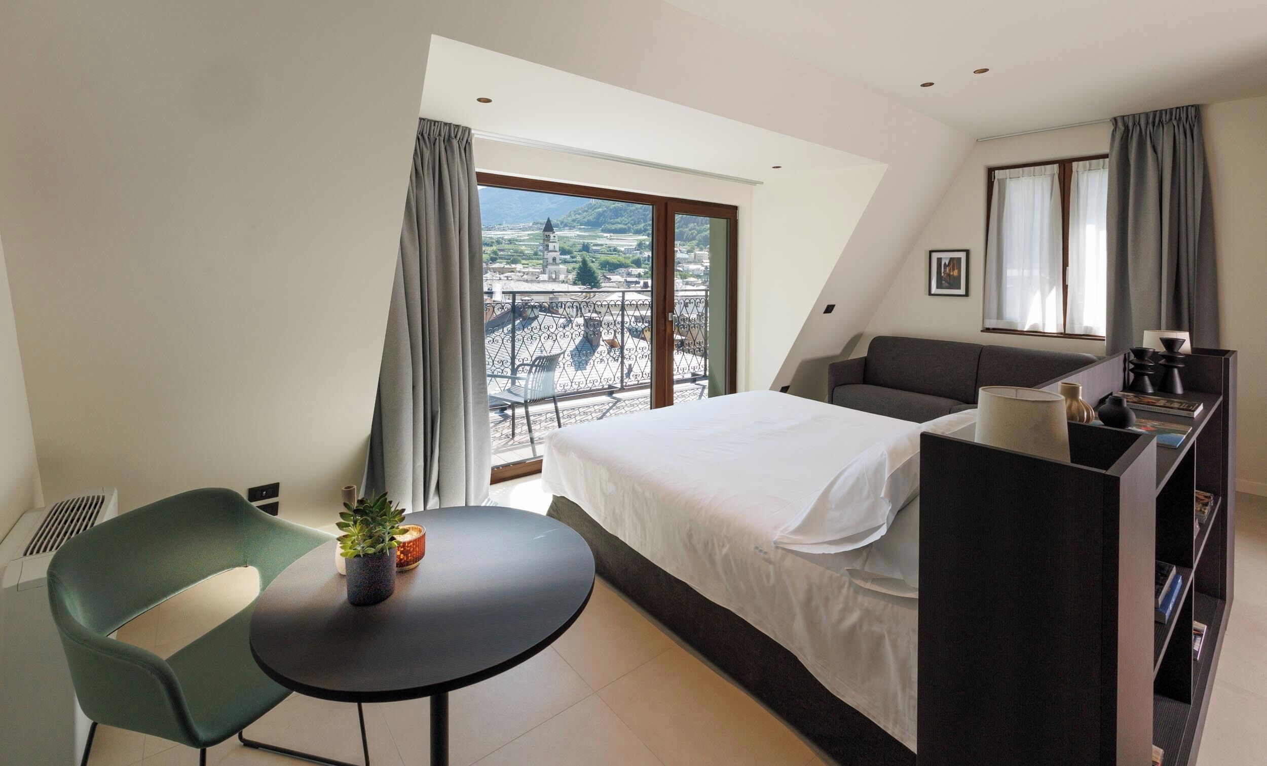 Ein modernes Hotelzimmer mit Bett, Schreibtisch, Stuhl und einem Balkon mit Blick auf eine Stadtlandschaft.