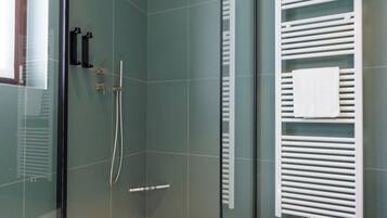 Een moderne douche met een glazen deur, een handdouche en een witte handdoekhouder.