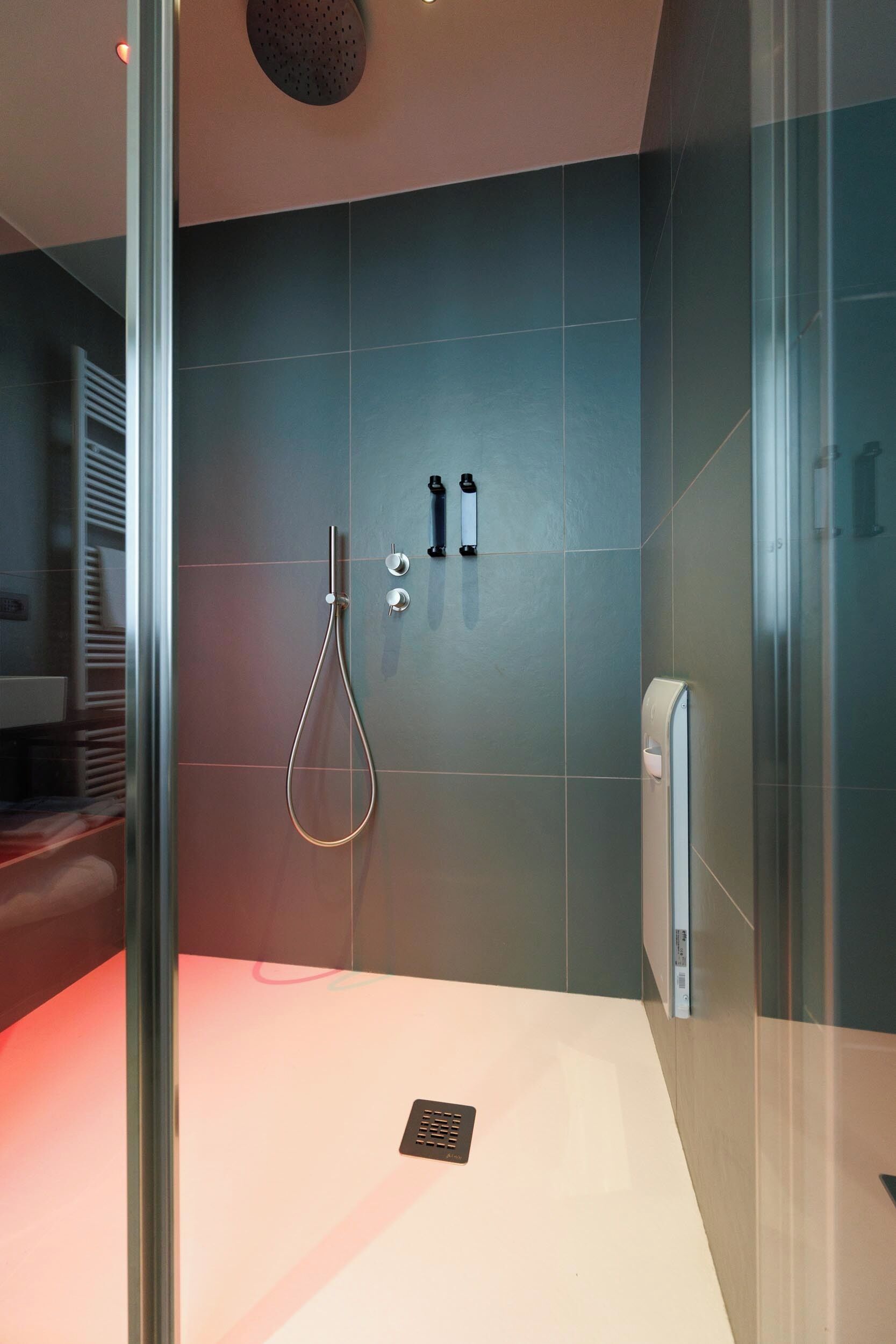 A modern bathroom with a glass shower enclosure, a white sink, and a wall-mounted towel dispenser.