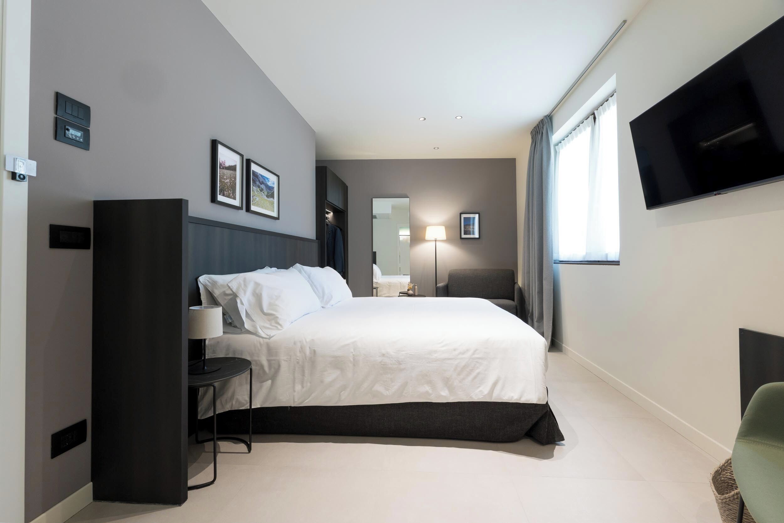 Una habitación de hotel moderna con una cama grande, un televisor de pantalla plana, una mesita de noche y una silla.