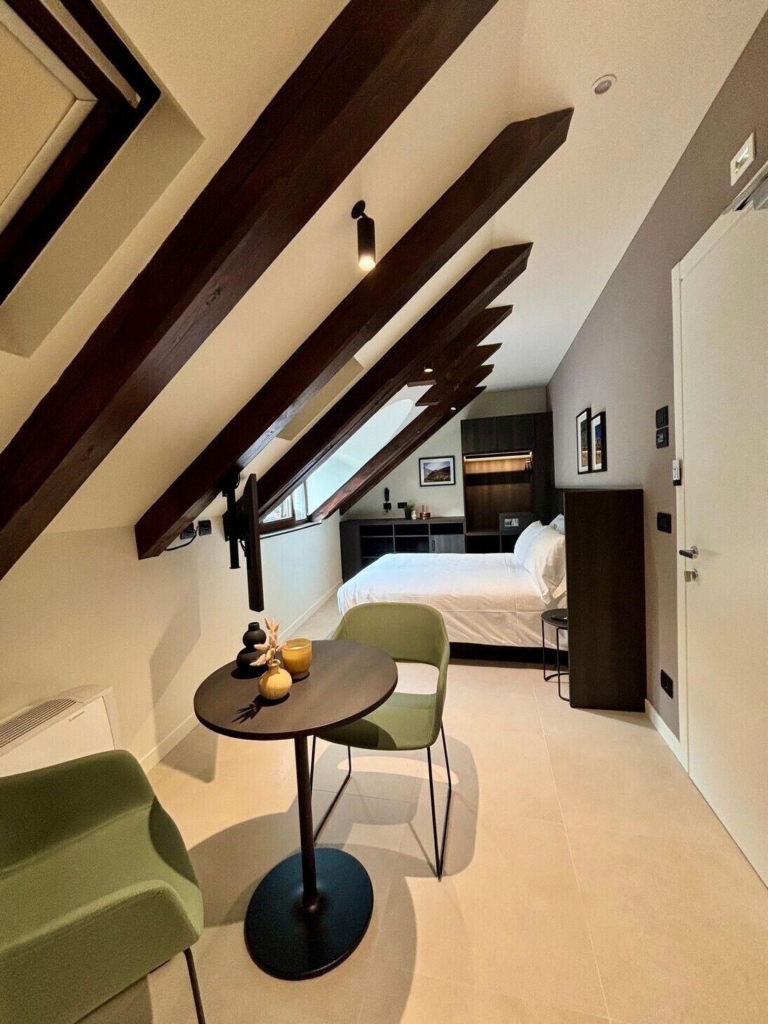 Una habitación compacta con techo inclinado, una cama, una mesita con adornos y una silla verde.