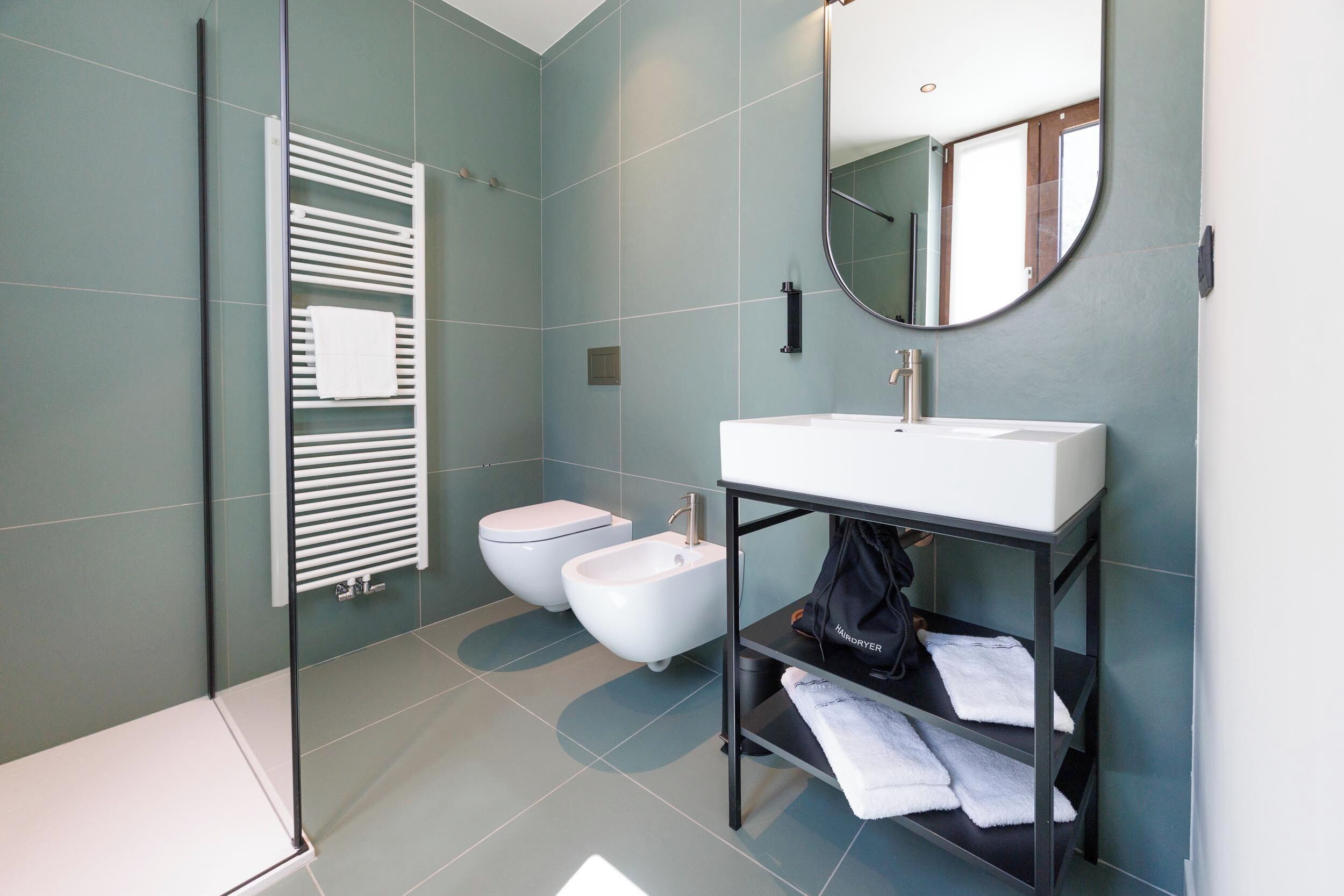 Casa de banho moderna com lavatório branco, bidé e cabine de duche em vidro.