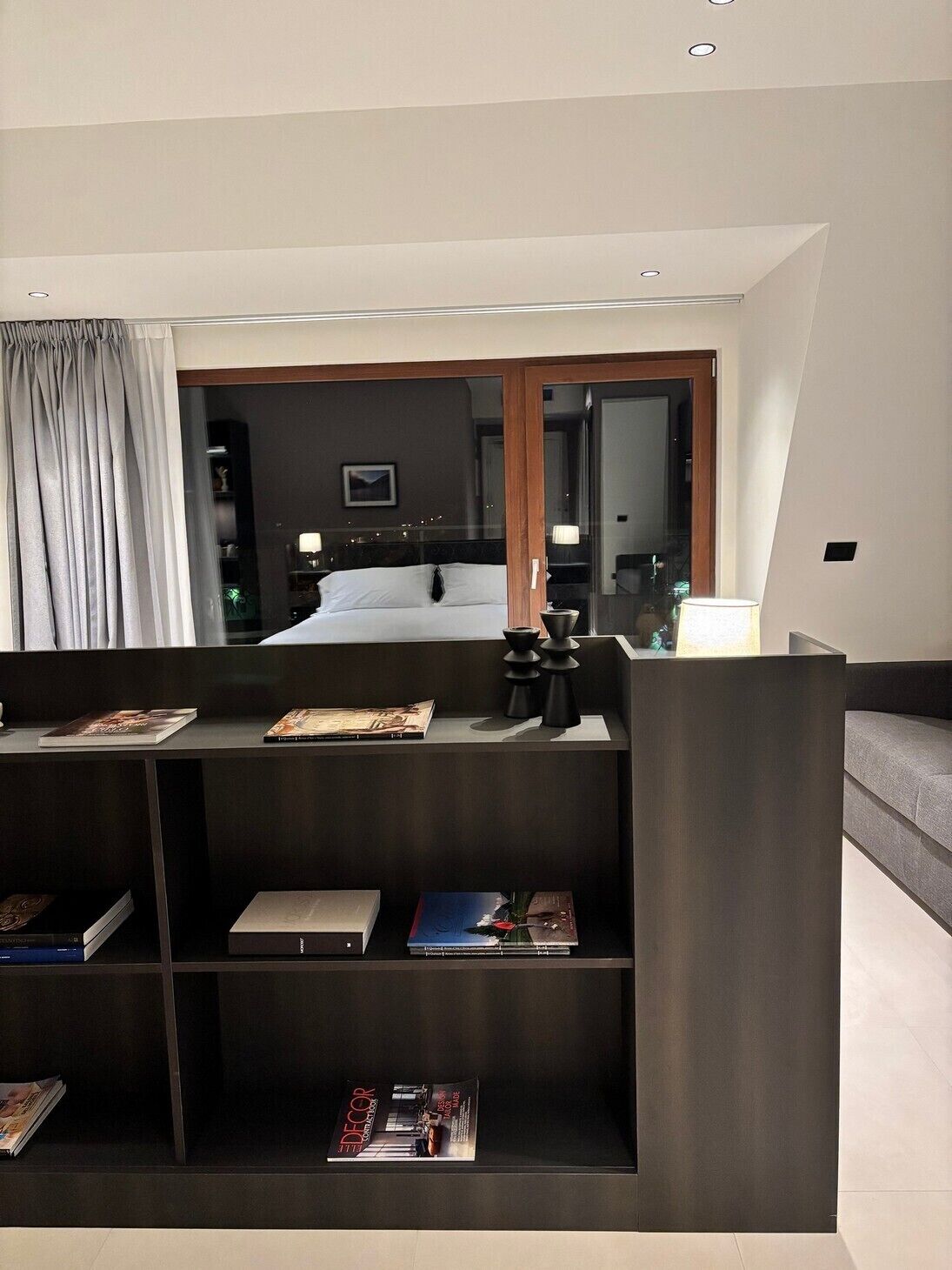 Una habitación de hotel moderna con una cama grande, un escritorio con lámpara y una estantería con revistas.