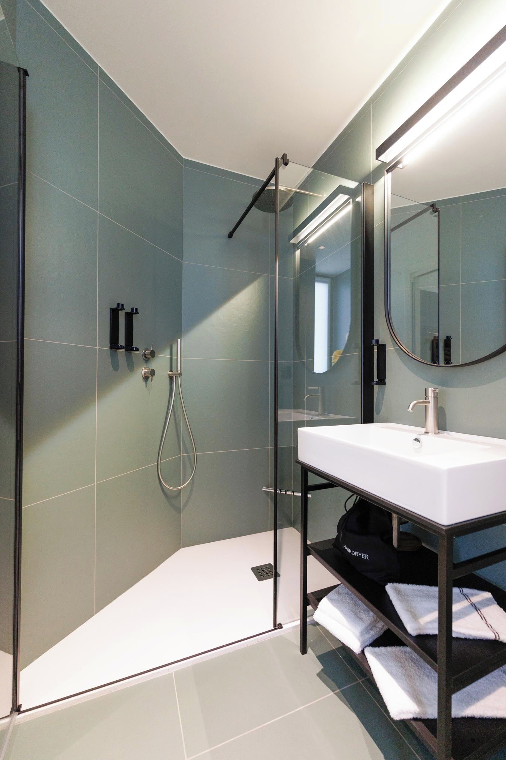 Un baño moderno con ducha acristalada, lavamanos blanco y espejo.