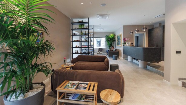 A modern living room with a sofa, a coffee table, a bookshelf, and a large potted plant. - Hotel Stelvio Tirano (Tirano)