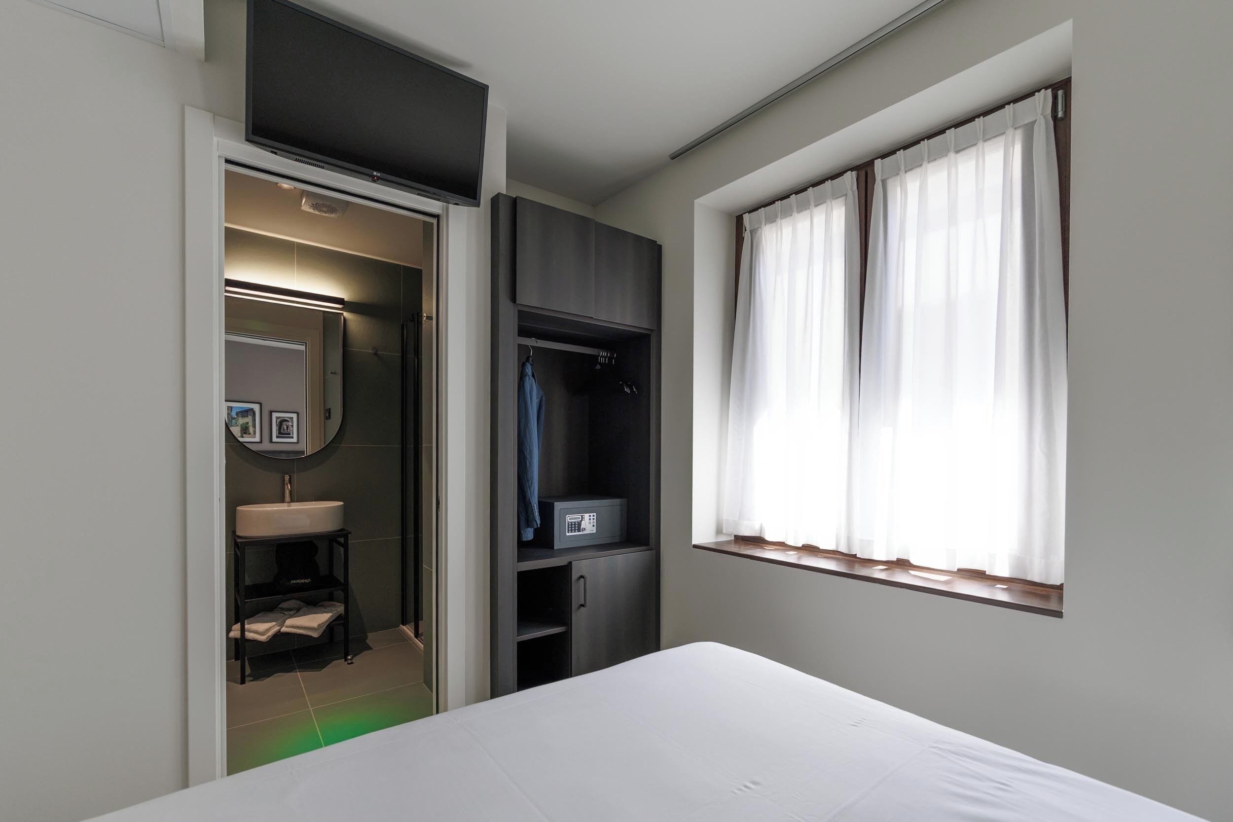A bedroom with a bed, a wardrobe, a mirror, and a window with curtains.