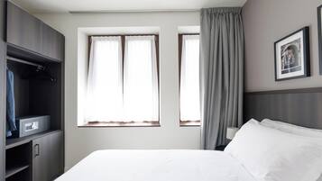 Habitación de hotel con cama, armario, dos ventanas con cortinas y un cuadro en la pared.