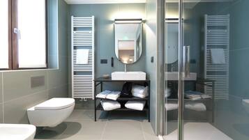 A modern bathroom with a white toilet, a large sink, and a glass shower enclosure. There are towel racks and a mirror above the sink.