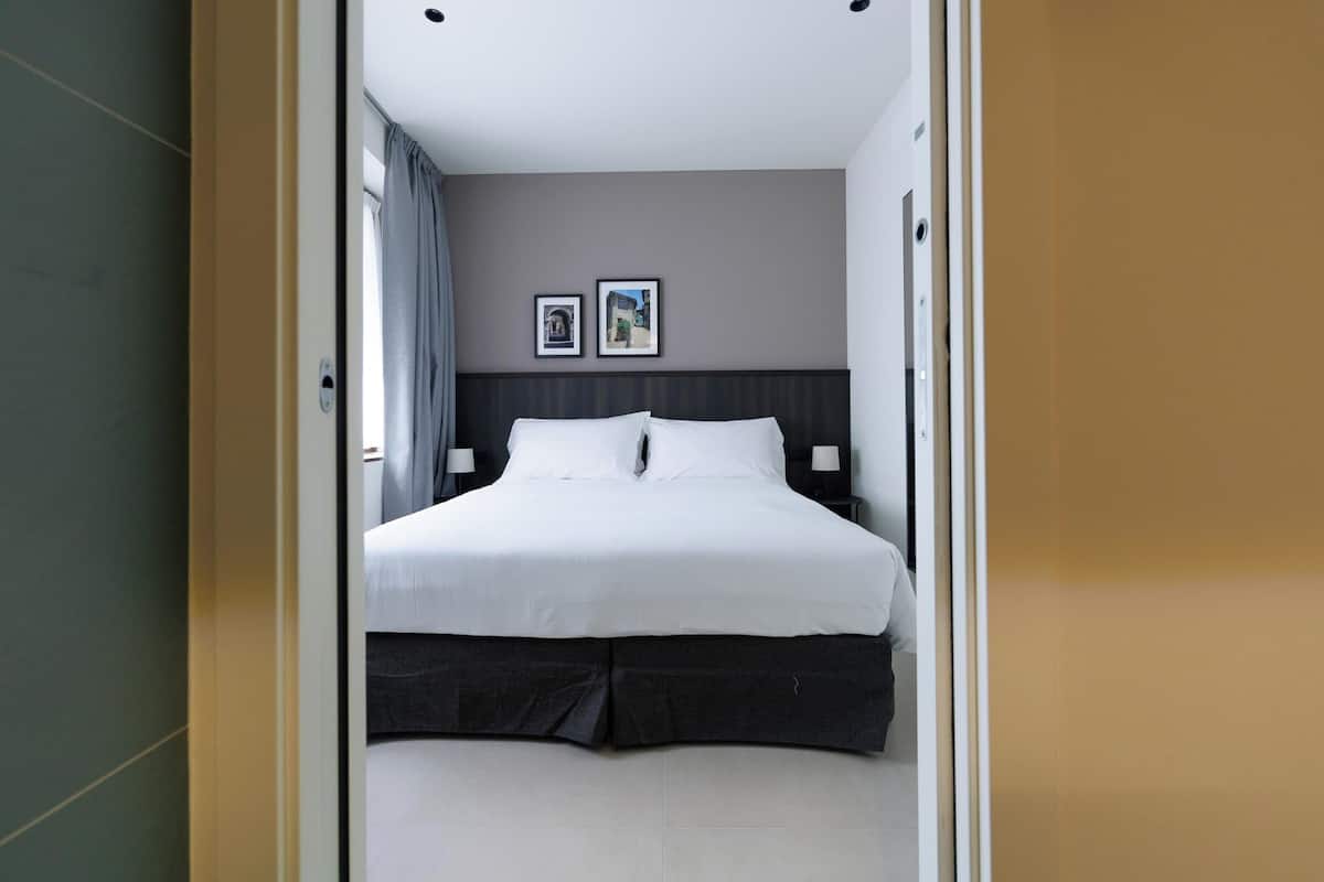 Una habitación de hotel moderna con una cama grande, un cabecero oscuro y dos cuadros enmarcados en la pared.