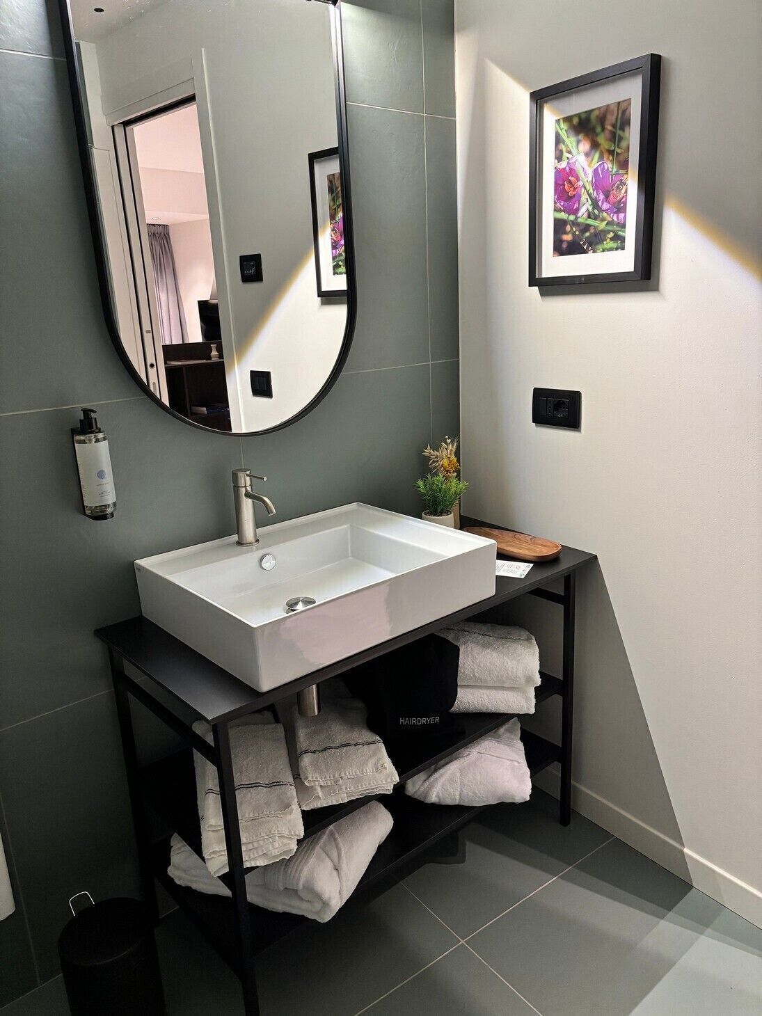 Un baño moderno con un lavamanos grande blanco, un espejo, un cuadro enmarcado en la pared y un estante con toallas.