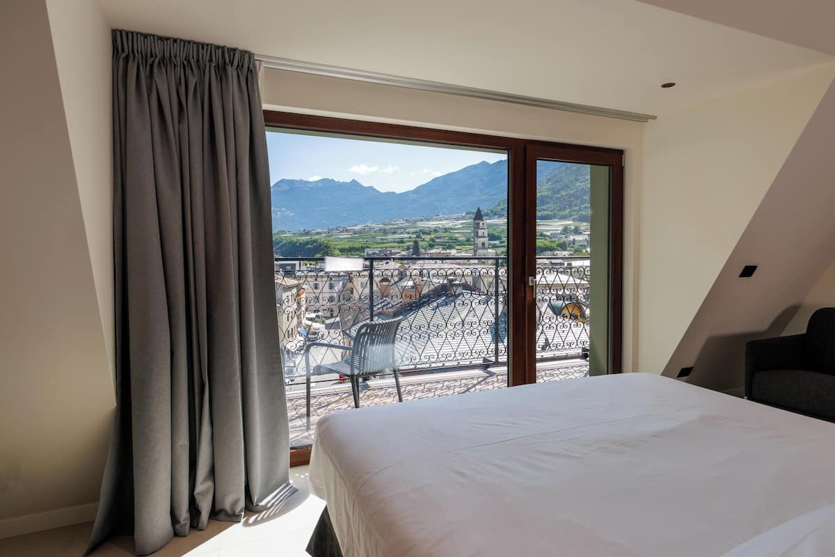 Un dormitorio con una cama grande, vistas a montañas y un balcón con barandilla.