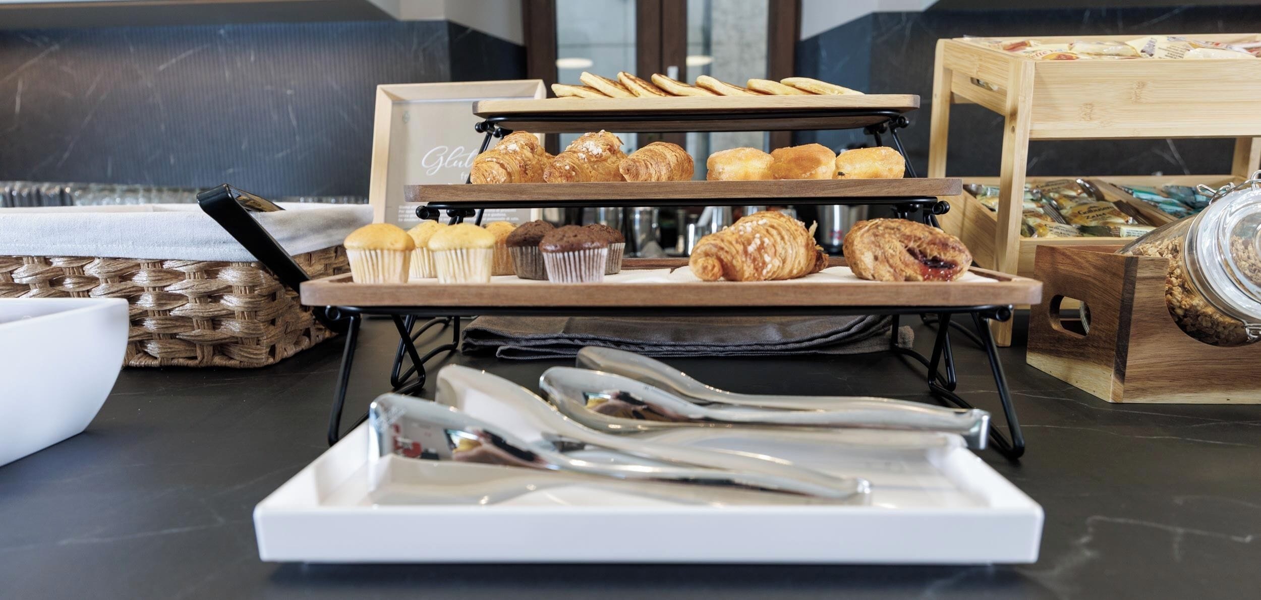 Un bufé de desayuno con pastelería, muffins y una variedad de alimentos expuestos en pedestales de madera.