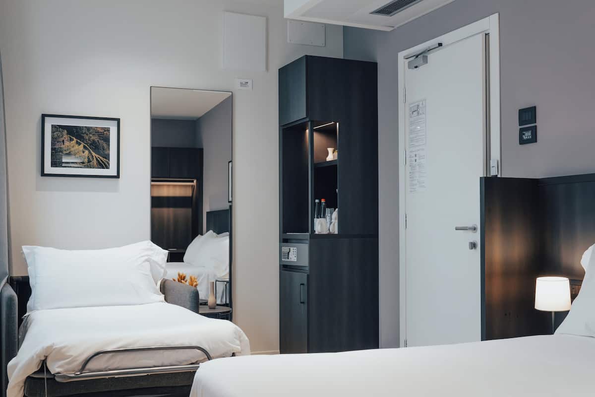 Habitación de hotel con cama, mesita de noche, espejo, armario y un cuadro en la pared.